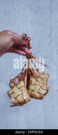 Eine Hand von Frau hielt gekochtes Ketupat oder südostasiatische Reiskuchen-Bündel, oft für Festlichkeiten zubereitet und sehr populäres Gericht während Eid Mubarak cel Stockfoto