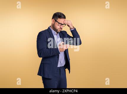 Besorgter junger Geschäftsmann, der den Kopf in Stress berührt, während er Rezessionsnachrichten über das Handy liest. Männlicher Profi in Vollanzug mit Cellpho gekleidet Stockfoto