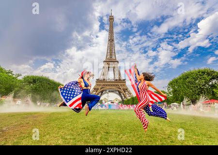 Patriotische Amerikanerin springt und jubelt für das Team USA und die Olympischen Spiele 2024 in Paris vor dem Eiffelturm, Paris, Frankreich, Europa Copyright: Stockfoto