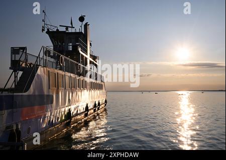 Fähre von der Halbinsel Tihany auf der ruhigen Wasseroberfläche des Sees Balaton mit Sonnenaufgang und kleinen Fischerbooten Stockfoto