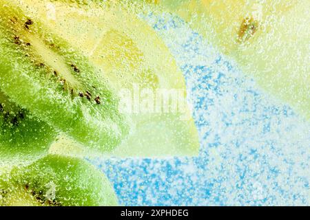 Saftige Kiwi- und Zitronenscheiben in spritzigem Wasser, die erfrischende tropische Leckerbissen vor blauem Hintergrund einfangen. Strukturierte Tapete. Stockfoto