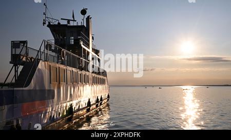 Fähre von der Halbinsel Tihany auf der ruhigen Wasseroberfläche des Balaton-Sees mit Sonnenaufgang und kleinen Fischerbooten im Breitbildformat Stockfoto