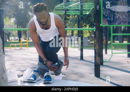Ein junger schwarzer Mann mit Bart und Dreadlocks steht im Park und zieht sich vor dem Training aus, um sich auf das Calisthenics vorzubereiten. Stockfoto