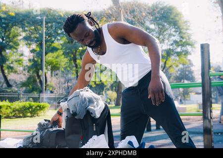 Junger afrikanischer Mann in Sportbekleidung bereitet sich auf Sport im Park vor, er legt seine Sachen auf die Bank. Stockfoto