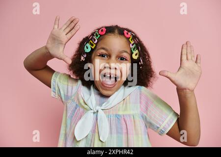 Ein junges afroamerikanisches Mädchen mit bunten Haarspangen lächelt in einem pastellfarbenen Kleid. Stockfoto