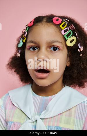 Ein junges afroamerikanisches Mädchen mit bunten Haarspangen steht vor einem rosafarbenen Hintergrund. Stockfoto