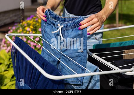 Die Frau hängt draußen die Wäsche auf einem Kleiderständer im Garten auf. Hausarbeiten Stockfoto
