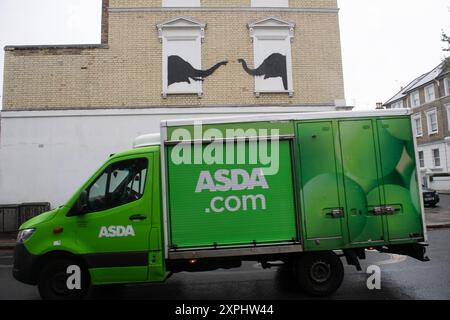 London, Großbritannien. August 2024. Ein ASDA-Lieferwagen fährt an einem neuen Wandgemälde des Street-Künstlers Banksy vorbei, das zwei Elefanten in Fensterbänken zeigt, das in Chesea enthüllt wurde. Quelle: Justin Ng/Alamy Live News Stockfoto