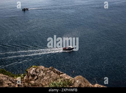 Kleine Freizeitboote, die Polperro verlassen, hinterlassen eine Spur von weißem Wasser in ihrem Gefolge. Blaues, ruhiges Wasser befördern Passagiere auf kurzen Touren durch die Bucht Stockfoto