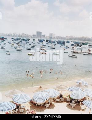 Ein lebhafter Yachthafen im östlichen Hafenbecken in Alexandria, Ägypten, Afrika, wurde im Juni 2006 eingenommen. Die Szene zeigt zahlreiche Boote, die im Wasser ankern, und Menschen, die den Strand unter Sonnenschirmen genießen. Stockfoto