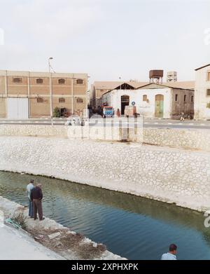 Depots und Lagerhäuser am Mahmoudiya-Kanal in der Nähe des Frachthafens in Alexandria, Ägypten. Bild im Juni 2006, die städtische und industrielle Architektur am Wasser, mit Menschen und Fahrzeugen darstellt. Stockfoto