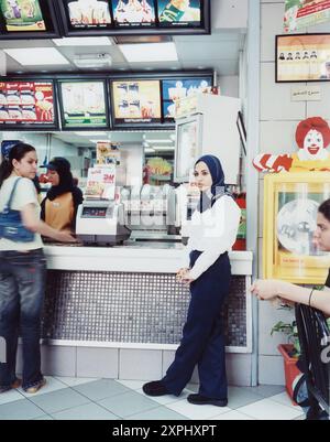 Innenansicht eines Fast-Food-Restaurants in Alexandria, Ägypten. Gäste und Mitarbeiter interagieren am Schalter mit Menütafeln und einem Ronald McDonald Display. Aufgenommen im Juni 2006. Stockfoto