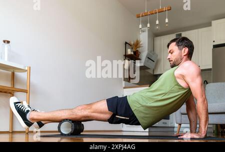 Mann, der zu Hause mit einer Schaumwalze eine selbstmyofasziale Freisetzungsübung durchführt. Stockfoto