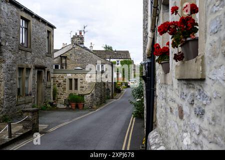 Grassington Yorkshire Großbritannien - 27. Juli 2024. Malerische Kopfsteinpflasterstraße in einem historischen Dorf mit Steinhäusern und leuchtenden roten Blumen. Stockfoto