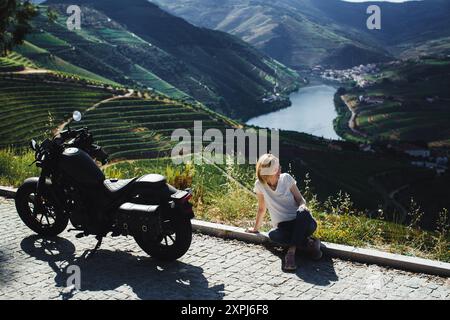 Eine Frau, die am Straßenrand vor dem Hintergrund der von Weinbergen bedeckten Hügel im Douro-Tal, Portugal, sitzt. Stockfoto