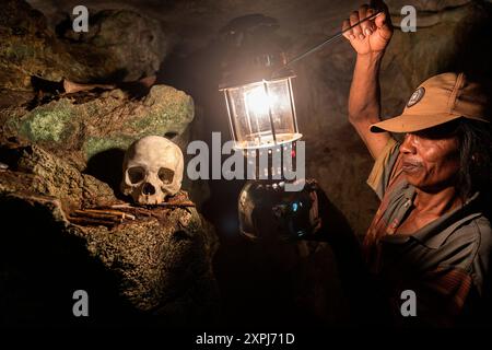 Ein Reiseleiter mit einer Laterne beleuchtet einen menschlichen Schädel in einer Höhle auf dem antiken Friedhof Londa, dem Höhlenfriedhof Toraja, Tana Toraja, Sulawesi, Indonesien Stockfoto