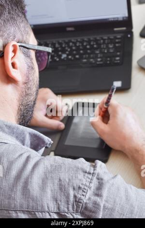Junger Mann, der vor seinem Laptop auf einem Tablet für die Datenanalyse schreibt. Stockfoto
