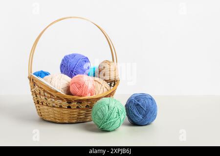 Viele bunte Strickbälle im Korb mit Stricknadeln auf grauem Hintergrund. Set für das Hobbys, warme Kleidung oder Spielzeug zu stricken. Konzeptnadelarbeit Stockfoto