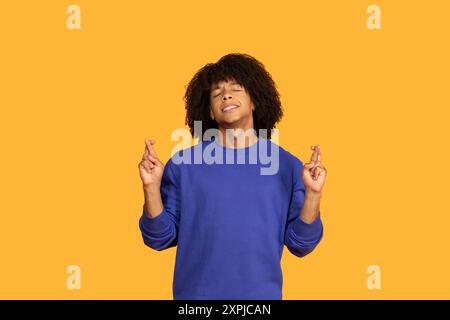 Junger Mann mit lockigen Haaren, die lächeln und die Finger kreuzen Stockfoto