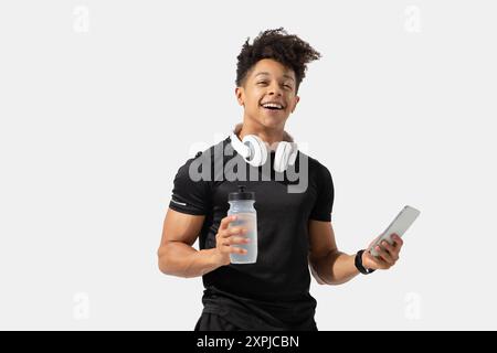 Mann in Aktivkleidung lächelt, während er Wasserflasche und Smartphone hält Stockfoto