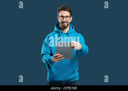 Junger Mann In Blauem Hoodie, Der Ein Tablet Hält Und Lächelt Stockfoto
