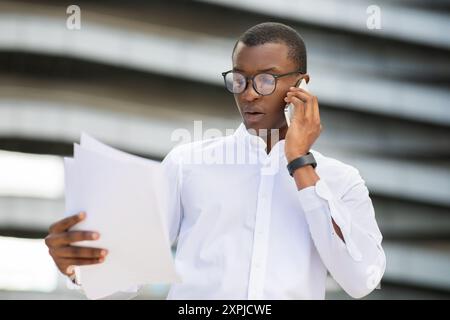 Junger Geschäftsmann, der Dokumente hält, während er draußen telefoniert Stockfoto