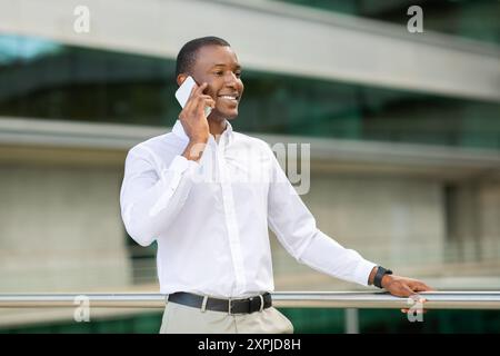 Professioneller Mann, der sich in Telefongesprächen vor dem modernen Glasgebäude verwickelt hat Stockfoto