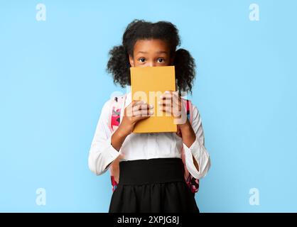 Shy African American Schulmädchen Versteckt Hinter Buch, Studio Shot Stockfoto