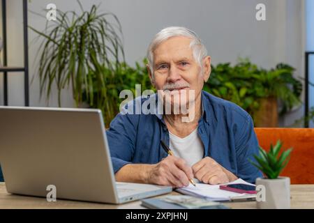 Senior man Buchhaltungszahlungen berechnen monatliche Ausgaben Bankrechnungen analysieren Papierkram in der Wohnung drinnen. Alter alter Großvater Freiberufler, der Online-Remote-Job am Laptop am Tisch arbeitet Stockfoto