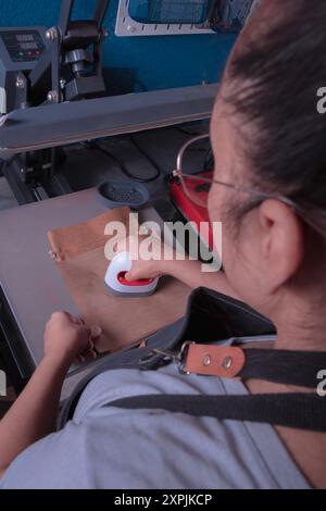 Die junge arbeitende Frau in ihrer Werkstatt macht den Sublimationsprozess mit einem Etikettenschild-, Druck- und Grafikdesign-Konzept. Stockfoto