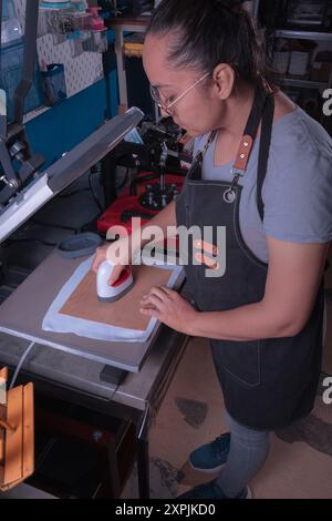 Die junge arbeitende Frau in ihrer Werkstatt macht den Sublimationsprozess mit einem Etikettenschild-, Druck- und Grafikdesign-Konzept. Stockfoto