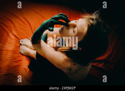 Ein Mädchen mit langen Haaren und geschlossenen Augen, ein schwarzes Kleid mit dämonischen Händen, sitzt auf einem roten Hintergrund. Die Szene ist voller Mystik und Andeutungen von H Stockfoto