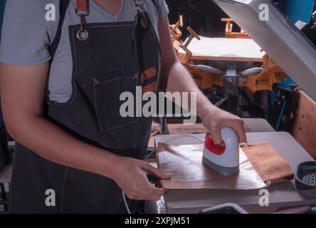 Die junge arbeitende Frau in ihrer Werkstatt macht den Sublimationsprozess mit einem Etikettenschild-, Druck- und Grafikdesign-Konzept. Stockfoto