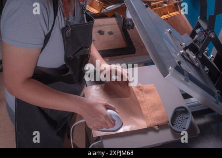 Die junge arbeitende Frau in ihrer Werkstatt macht den Sublimationsprozess mit einem Etikettenschild-, Druck- und Grafikdesign-Konzept. Stockfoto
