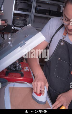 Die junge arbeitende Frau in ihrer Werkstatt macht den Sublimationsprozess mit einem Etikettenschild-, Druck- und Grafikdesign-Konzept. Stockfoto
