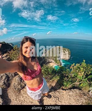 Eine Frau in einem roten Bikini macht ein Selfie auf einer Klippe mit Blick auf den Ozean. Konzept von Abenteuer und Spannung, während die Frau für ein Foto posiert i Stockfoto