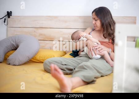 Eine Frau mit einem Neugeborenen in den Armen liegt auf dem Bett in ihrem Zimmer, um sie einzuschlafen. Stockfoto