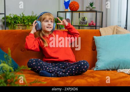 Glückliches, überfreudiges Teenager-Mädchen Kind in kabellosen Kopfhörern sitzt entspannt auf dem Sofa zu Hause und hört energiegeladene Disco-Tanzmusik. Freizeitaktivitäten für Kinder am Wochenende. Lebensstil Stockfoto