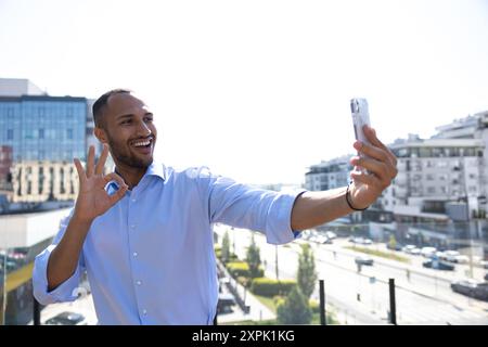 Lächelnder junger Geschäftsmann, der in der Stadt ein Mobiltelefon benutzt und Videoanrufe führt Stockfoto