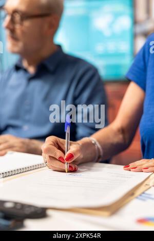 Reife Frau, die den Lebensversicherungsvertrag mit der Beraterin unterzeichnet, um ihren Ruhestand und ihre Ersparnisse zu sichern. Unterschrift des Dokuments für die künftige Finanzstabilität. Nahaufnahme. Stockfoto