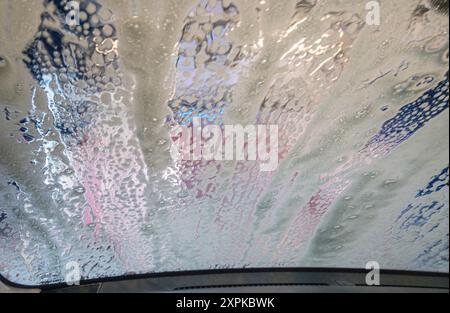 Die Windschutzscheibe eines Autos, das durch eine automatische Waschanlage fährt. Das Fenster wird mit Seife bedeckt, wenn der Waschvorgang beginnt. Stockfoto