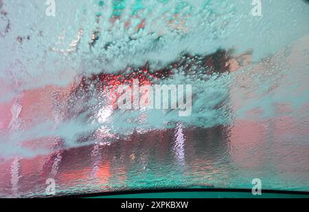 Die Windschutzscheibe eines Autos, das durch eine automatische Waschanlage fährt. Das Fenster ist mit Seife bedeckt, wenn es während des Spülzyklus entfernt wird. Stockfoto