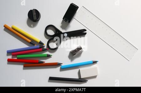 Foto der Büroausstattung. Zufällig auf weißem Hintergrund verstreut. Farbstifte, Scheren, Hefter, Radierer, Spitzer, Regeln. Farbige Bleistifte haben schwarzes Holz. Zurück zur Schule. Stockfoto