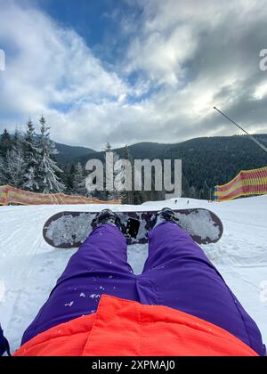 Frau, die mit Snowboard auf Schnee liegt Stockfoto