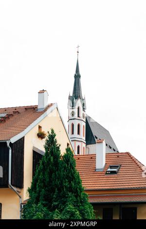 Ein markanter Kirchturm mit einem hohen Turm dominiert die Skyline eines bezaubernden europäischen Dorfes. Traditionelle Häuser mit Terrakottadächern umgeben das Stockfoto