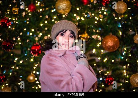 Russische 48-jährige Frau in rosa Mantel, die vor Neujahr vor weihnachtsbaum und Lichtern steht Stockfoto