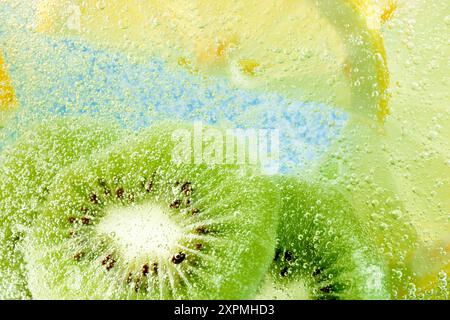 Saftige Kiwi- und Zitronenscheiben in spritzigem Wasser, die erfrischende tropische Leckerbissen vor blauem Hintergrund einfangen. Strukturierte Tapete. Stockfoto