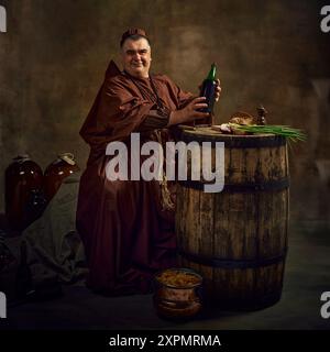 Reifer Mann, mittelalterlicher Mönch in alter Kleidung, der mit einem Lächeln sitzt und eine Flasche Bio-Wein vor Vintage-Hintergrund mit Holzfässern hält Stockfoto