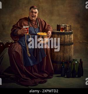 Fröhlicher Mann, mittelalterlicher Mönch, mit Bier, Bier und Chips, fröhlich vor Vintage-Hintergrund. Rustikale Klosteranlage Stockfoto