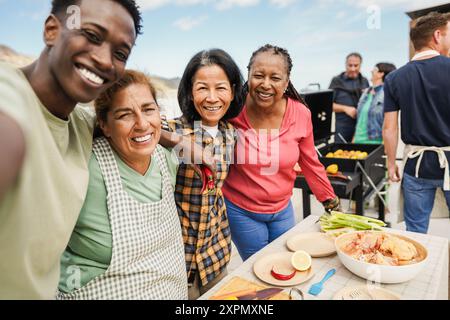 Generationenübergreifende Menschen, die auf dem Dach des Hauses grillen - multirassische Freunde, die am Wochenende Spaß beim Essen und Kochen haben - Sommer und Stockfoto